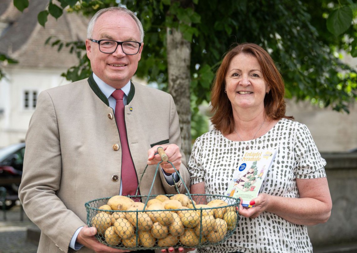 Landeshauptfrau-Stellvertreter Stephan Pernkopf hält gemeinsam mit "So schmeckt NÖ"-Leiterin einen Korb Erdäpfel und die Broschüre der Erdäpfelpyramide.