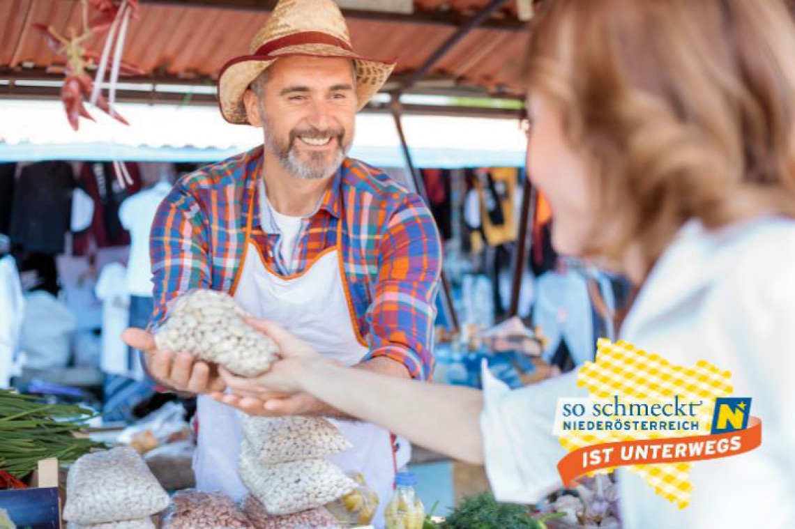 Produzent verkauft ein Sackerl Bohnen am Markt an eine Dame. Die Übergabe ist zu sehen.