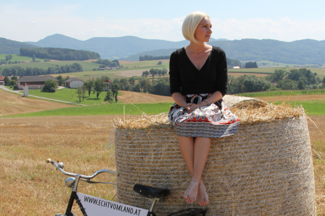 Diana Umgeher von "Echt vom Land" sitzt auf einem Heuballen auf einem Feld.