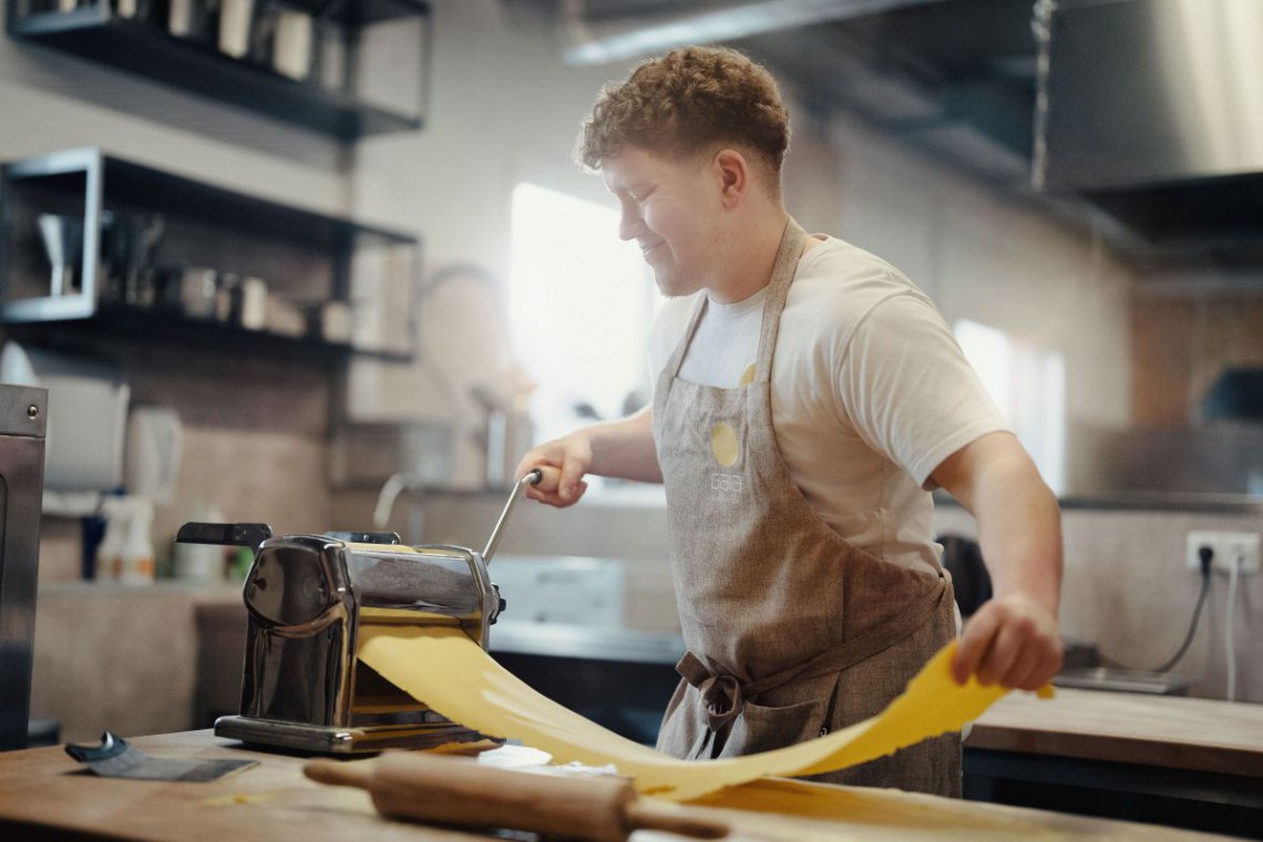 Mann rollt den Nudelteig durch eine Nudelmaschine aus
