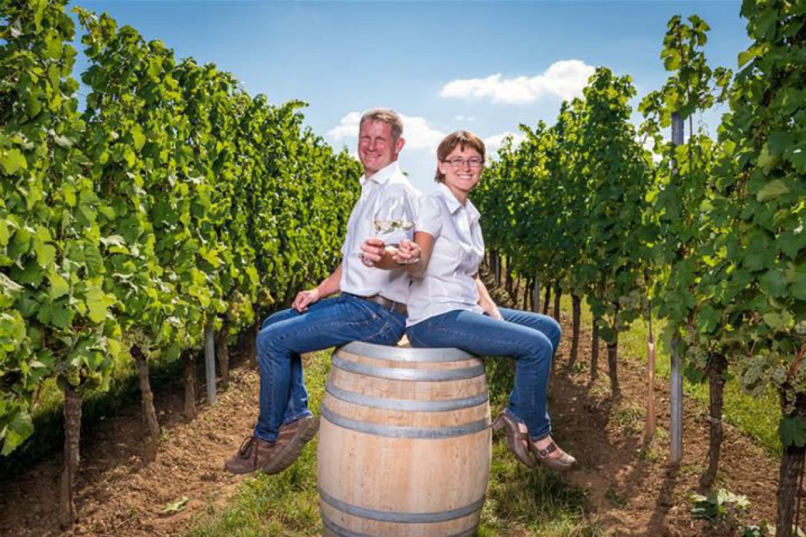 Herr und Frau Greillinger sitzen auf Weinfass im Weingarten