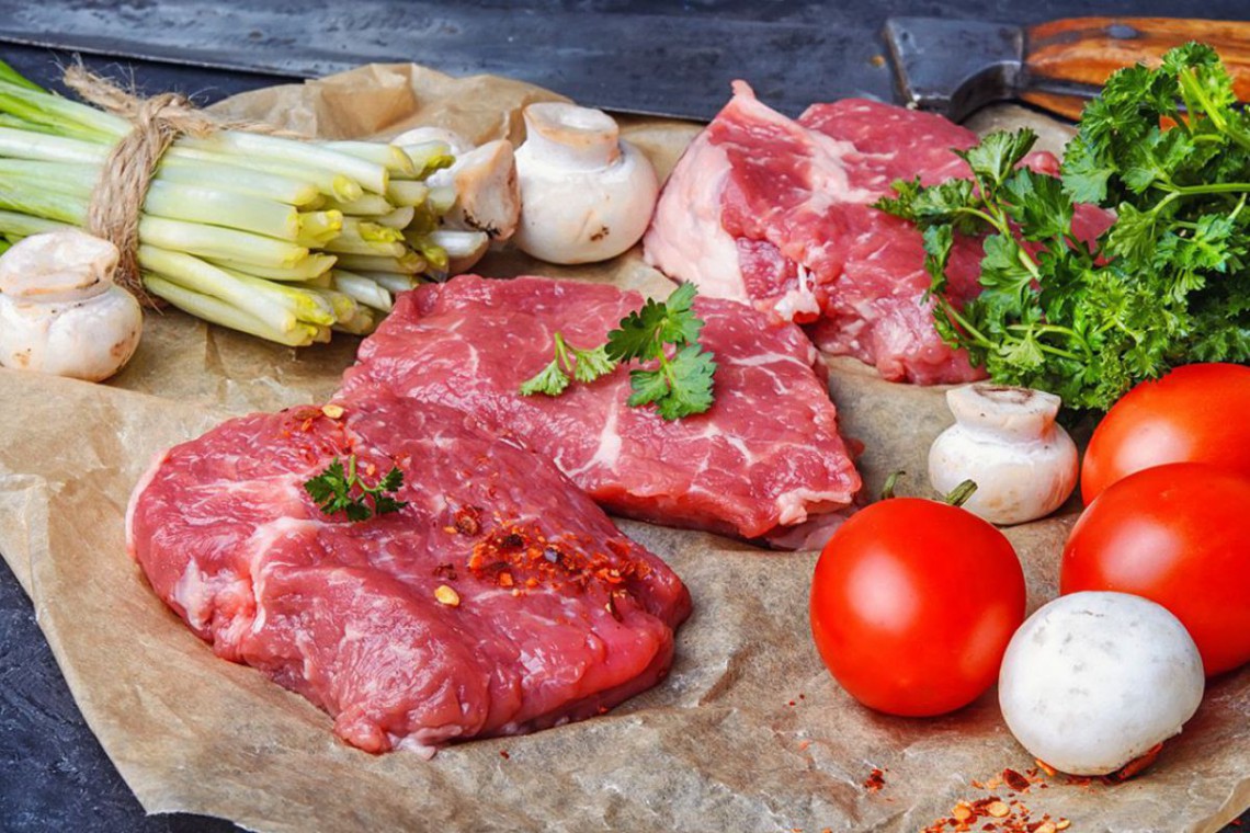 Rohes Fleisch neben Gemüse und Kräutern
