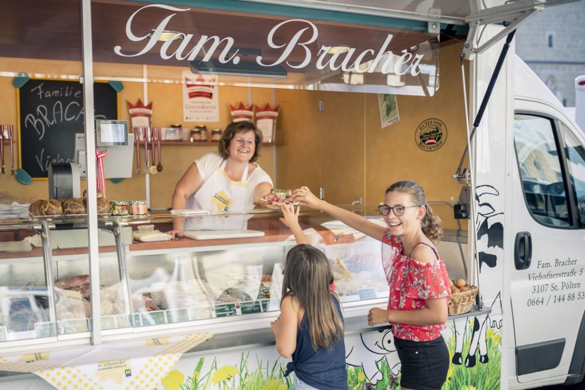 Zwei Kinder probieren Köstlichkeiten bei einem Bauernmarktstand