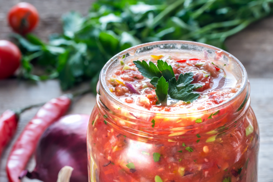 Ein Glas mit Zucchin-Chutney darin, im Hintergrund liegt Gemüse am Tisch