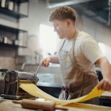 Bild anzeigen: Mann rollt den Nudelteig durch eine Nudelmaschine aus