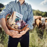 Bild anzeigen: Ein Korb voller Produkte in H&auml;nden gehalten auf einer Wiese mit K&uuml;hen