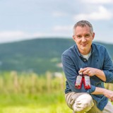 Bild anzeigen: Michael Priessnitz im Feld mit 2 Flaschen Sirup in der Hand