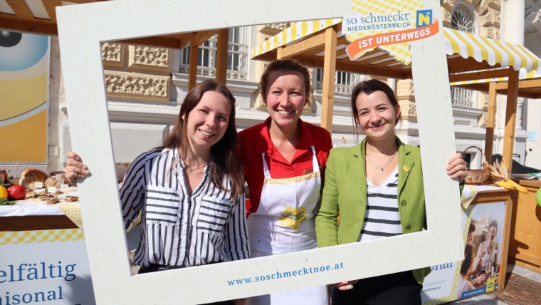 Gruppenfoto mit "So schmeckt NÖ"-Rahmen beim Tourstopp am Bauernmarkt in St. Pölten