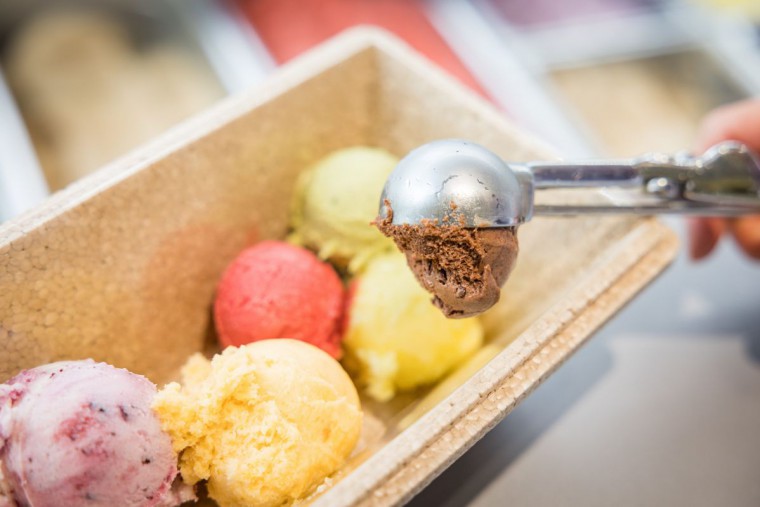 Eisverkäuferin füllt verschiedene Sorten Eiskugeln in eine Kühlbox.