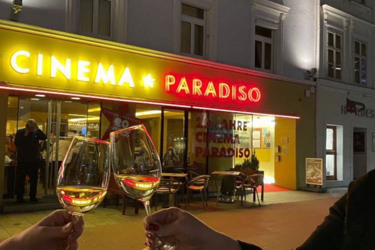 Cinema Paradiso St. Pölten im Hintergrund, davor stoßen zwei Menschen mit ihren Weingläsern an.