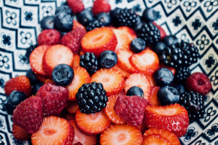Verschiedene frisch geschnittene Beeren wie Erdbeeren, Himbeeren, Brombeeren und Heidelbeeren in einer gemusterten Schale.