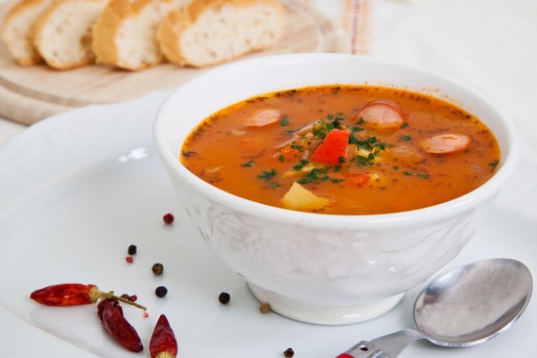 Eine Schüssel Kürbisgulasch mit Würstel, dazu Weißbrotscheiben