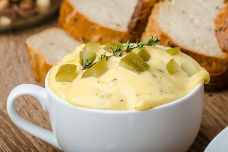 Mayonnaise in einer Tasse angerichtet vor einigen Scheiben Brot