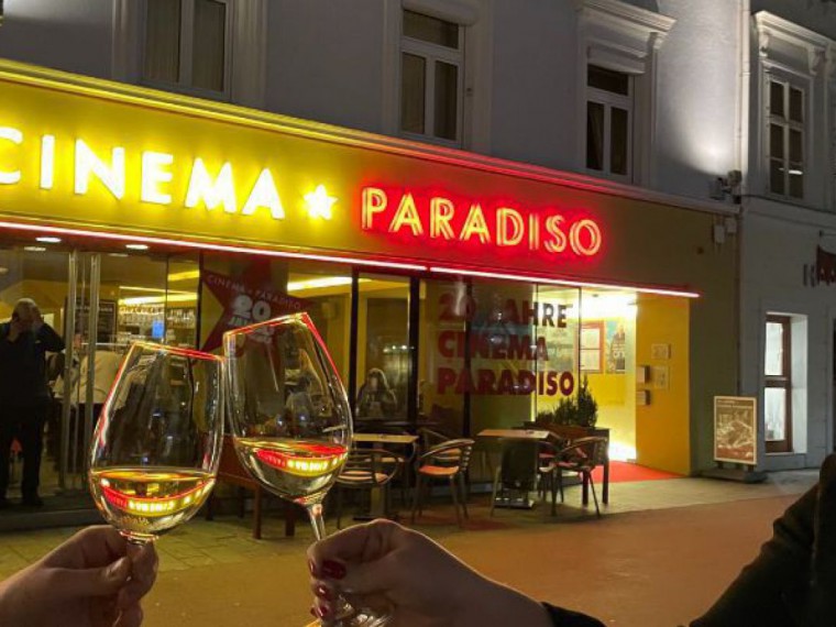 Cinema Paradiso St. Pölten im Hintergrund, davor stoßen zwei Menschen mit ihren Weingläsern an.