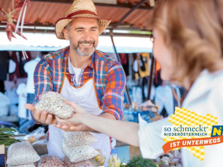 Produzent verkauft ein Sackerl Bohnen am Markt an eine Dame. Die Übergabe ist zu sehen.
