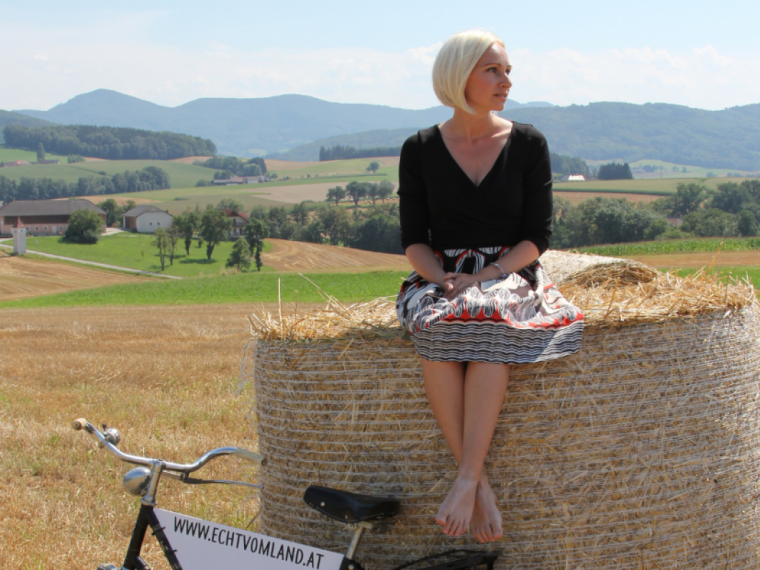 Diana Umgeher von "Echt vom Land" sitzt auf einem Heuballen auf einem Feld.