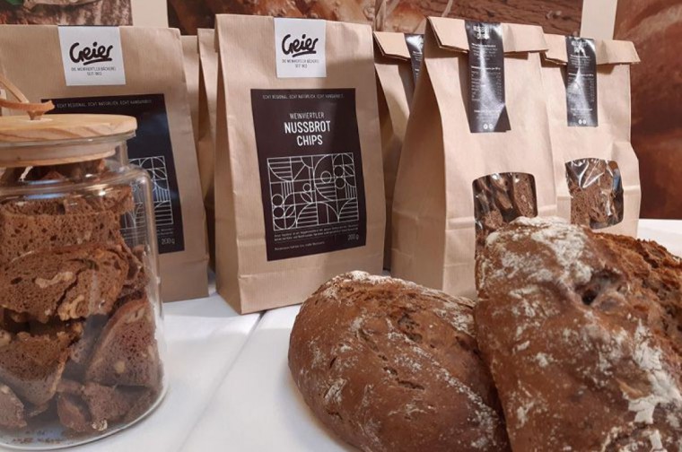 Altes Brot und Brotchips in Papiertüten auf einem weißen Tisch der Bäckerei Geier